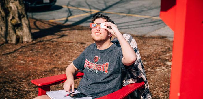 一位学生坐在椅子上，戴着日食眼镜凝视着太阳.